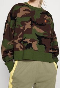 Camo sweatshirt featuring earth tones like green, brown, and black, with a ribbed neckline and hem, cropped design, and small logo detail.