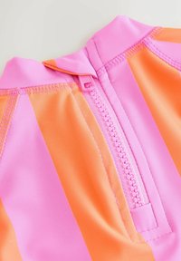 Rózsaszín és narancssárga csíkos fürdőruha magas gallérral, elöl cipzárral és sima, rugalmas anyaggal. Látható varrási részletek.