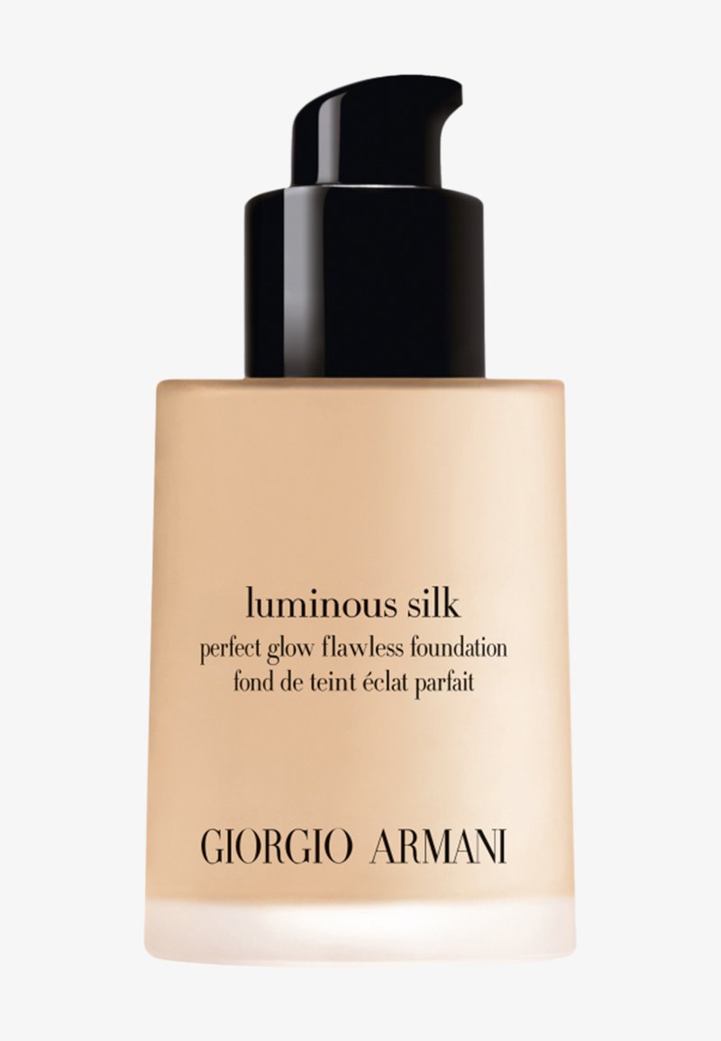 Flacone di fondotinta in vetro beige con pompa nera e etichetta con testo semplice che mostra il nome del prodotto e del marchio, texture liscia e design elegante.