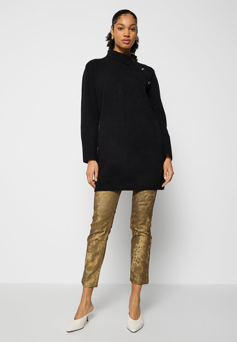 Maglione nero con colletto e due bottoni dorati, abbinato a pantaloni in stampa pitone dorata testurizzati e scarpe bianche con tacco alto.