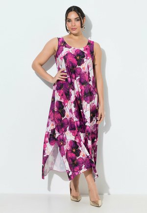 Donna con vestito midi senza maniche a fiori rosa e viola che posa con la mano sui fianchi su sfondo bianco.