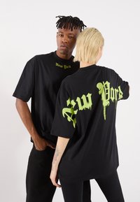 Tricouri negre supradimensionate cu „New York” imprimat în text de tip graffiti verde pe față și pe spate. Material din bumbac, design casual.