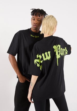 T-shirts oversize noirs avec "New York" imprimé en texte graffiti vert sur le devant et le dos. Matériau en coton, design décontracté.