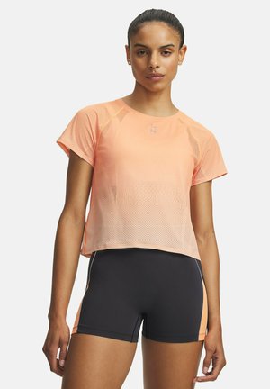 Vrouw staat rechtop en kijkt vooruit, draagt een perzikkleurig mesh kort mouwshirt en zwarte sportshorts met perzikkleurige zijpanelen op een witte achtergrond.