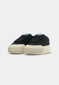 Sneakers neri con un upper in tela texturizzata, chiusura con lacci piatti e una suola chunky di colore crema; presenta un'etichetta con logo blu sulla linguetta.