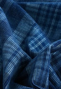 Denimstoff in verschiedenen Blautönen mit strukturierten Oberflächen. Enthält vertikale und horizontale Streifenmuster, die durchgehend eingewebt sind.