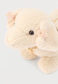 Sac peluche beige duveteux en forme de chien avec des yeux noirs, un nez crème et des accents de fleurs roses sur les oreilles. Doté d'une chaîne en or et d'une fermeture éclair.