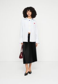 Svetlomodrá pruhovaná košeľa s gombíkmi s červenou srdcovou nášivkou, biely krátky top, čierna skladaná sukňa, bordová kabelka a čierne baleríny.