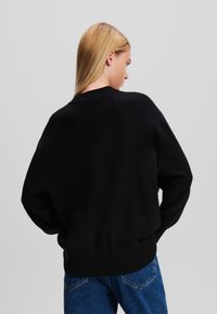 Fekete, oversize pulóver bordázott kerek nyakkivágással és passzoló bordázott aljjal. Puha tapintás, hanyagul ejtett vállakkal és laza szabással.