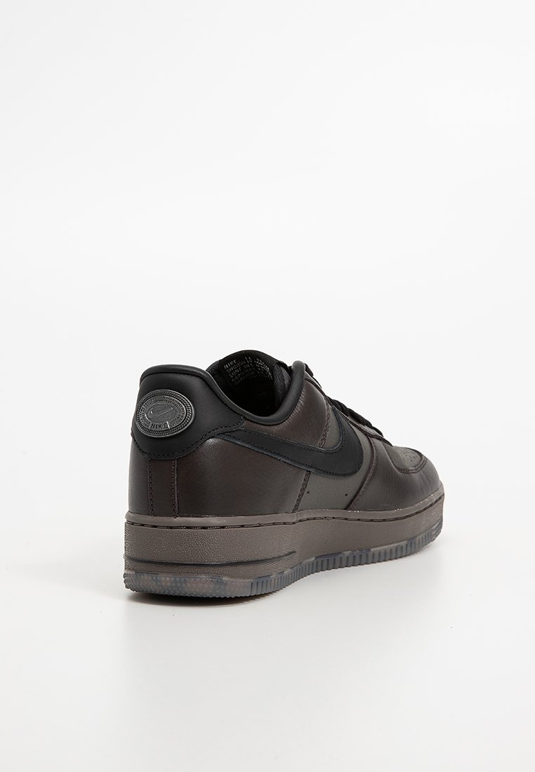 Zapatilla de cuero negro con acabado liso, que presenta una suela de goma oscura en contraste y un acento de logo circular en el talón.