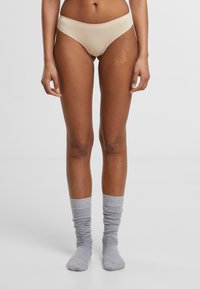 Bež donje rublje bez šavova s srednjim strukom, u kombinaciji s svijetlosivim rebrastim čarapama. Tkanina izgleda glatko i rastezljivo.