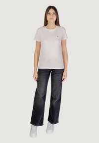 T-shirt rosa chiaro a maniche corte con un piccolo logo; abbinato a jeans scuri a vita alta e gamba larga e sneakers bianche.
