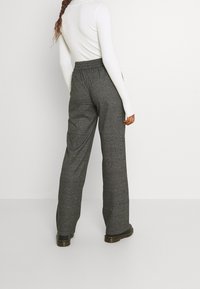 Pantalons à carreaux gris taille haute avec une coupe décontractée, dotés d'une taille élastique et de coutures visibles. Associés à un haut blanc à côtes.
