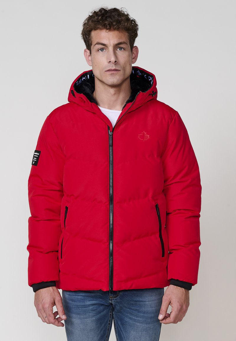 Chaqueta acolchada roja con capucha, cremallera frontal y detalles en negro. Presenta puños acanalados, dos bolsillos con cremallera y un logo en el pecho.