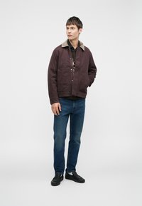 Lilla canvasjakke med krave, beige fleeceforing, foran trykknaplukning og to påsydde lommer. Båret med blå jeans og sorte sko.