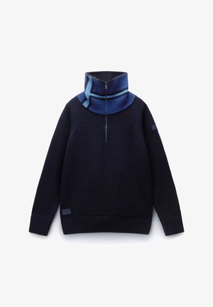 Pull en maille de couleur marine avec un col montant, des rayures dégradées bleues et une fermeture à demi-zip. Détails en bord-côte au niveau de l'ourlet et des poignets.
