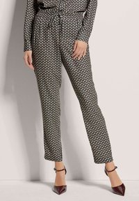 Zwarte broek met een patroon van diamanten in ivoor, voorzien van een elastische tailleband en een koorddetail. Gecombineerd met bordeauxrode puntige hakken.