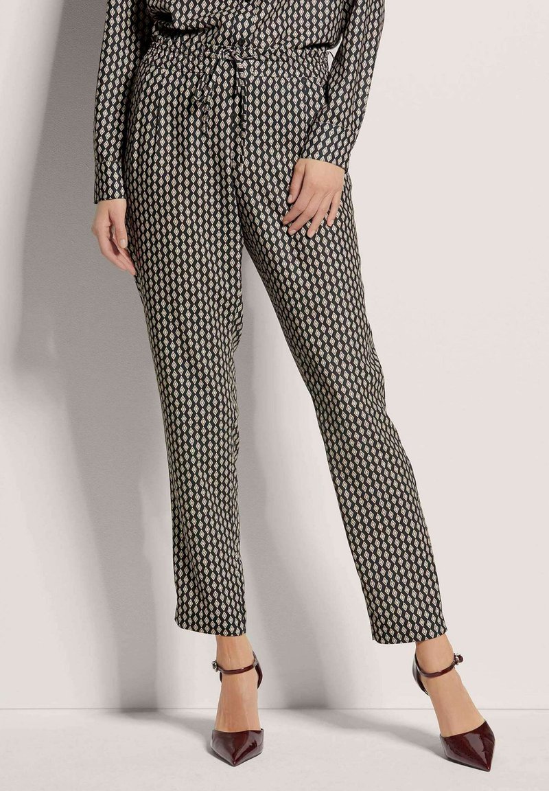 Zwarte broek met een patroon van diamanten in ivoor, voorzien van een elastische tailleband en een koorddetail. Gecombineerd met bordeauxrode puntige hakken.