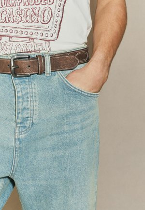 Light blue denim jeans with a relaxed fit, featuring a front pocket and a brown leather belt with a silver buckle.
