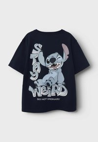 Navy krāsas kokvilnas t-krekls ar zīmējumu, kurā attēlots karikatūras varonis, un teksts "PALIEC DĪVAI" un "TĀ NAV PARASTA" kontrastējošās krāsās.