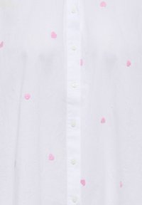 Chemise blanche boutonnée avec broderie de cœur rose. Présente une texture de tissu douce et un col classique, avec des boutons sur le devant.