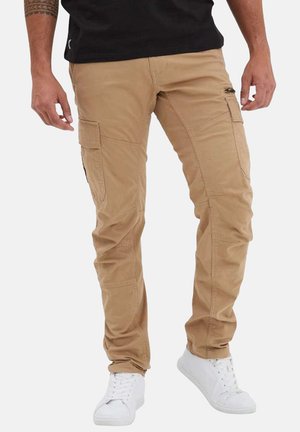 Pantalons cargo beiges à coupe slim, dotés de multiples poches et de détails cousus, associés à des baskets blanches. Conçus pour l'utilité et le confort.