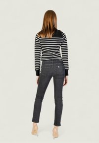 Top de manga larga a rayas en blanco y negro combinado con jeans negros ajustados, que cuentan con bolsillos traseros y un ligero desgaste. Tacones transparentes completan el look.