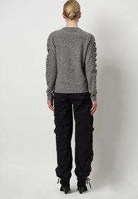 Grijze gebreide trui met gerimpelde details langs de mouwen, gecombineerd met zwarte cargobroek en enkellaarsjes met hak, gezien van achteren.