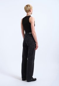 Black sleeveless top paired with high-waisted black jeans. Jeans feature a straight-leg cut and minimalistic detailing. Flat black shoes.