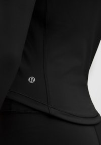 Top sport negru din material elastic, cu o croială ajustată, cusături plate și un logo mic pe partea stângă, aproape de margine.