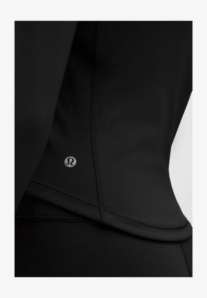Haut de sport noir en tissu extensible, avec une coupe ajustée, des coutures flatlock et un petit logo sur le côté gauche près de l'ourlet.