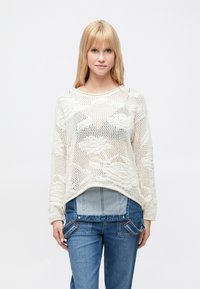 Pull crème en maille avec un tissage lâche et ouvert et des épaules tombantes, associé à une salopette en denim bleu avec des détails de poches.