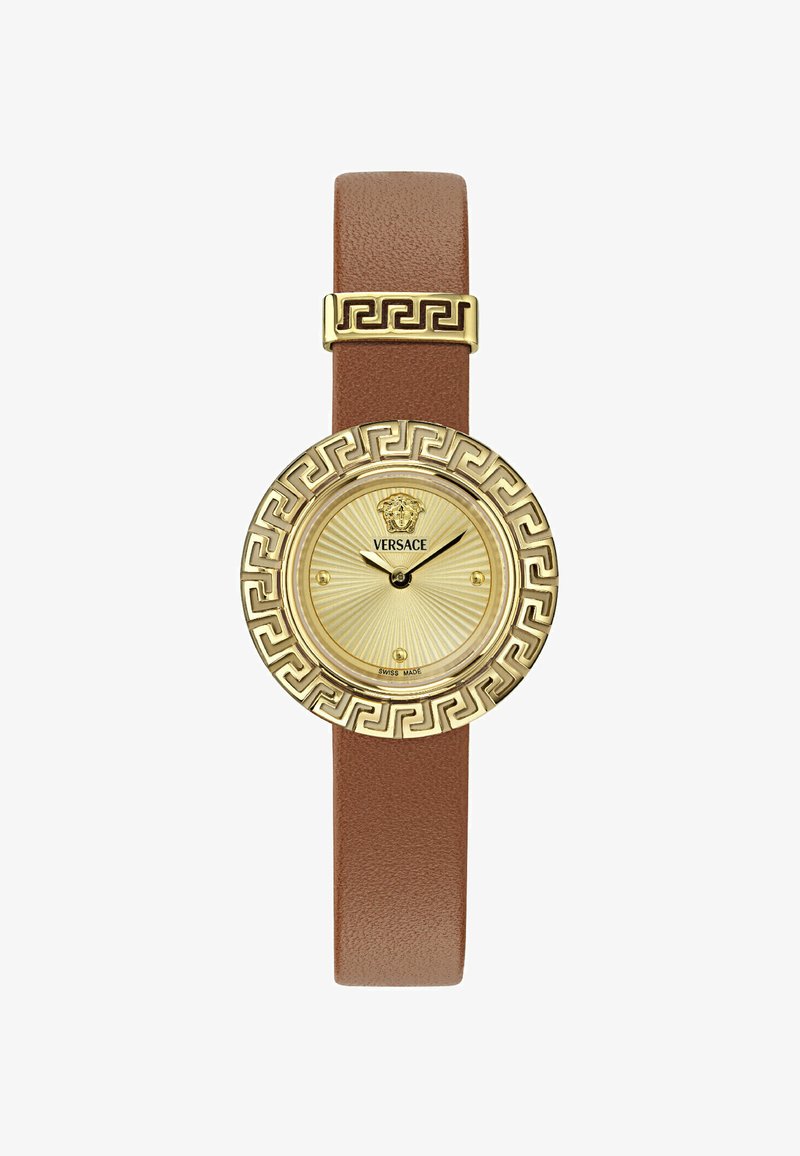 Kuldtoonelis kell, millel on ümmargune kellakujundus, tekstuuriga kuldne nägu ja pruun nahkraha. Dekoratiivne Kreeka võtme muster kellakorpuse peal.