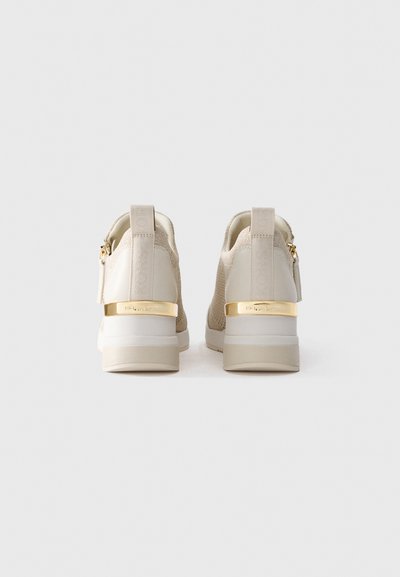 Une paire de baskets montantes beiges en tissu tricoté, avec des accents dorés au talon, des détails de fermeture éclair et des boucles au talon portant la marque, vues de l'arrière.