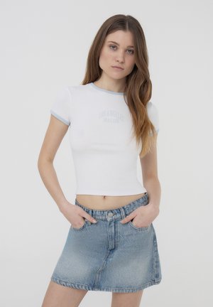 Maglietta bianca a maniche corte con colletto e polsini blu chiaro, con una grafica sbiadita "Los Angeles Malibu." Abbinata a una gonna in denim blu chiaro.