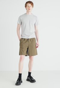 Grijze tshirt met korte mouwen, khaki shorts met elastische tailleband en zwarte schoenen, gecombineerd met zwarte sokken, tegen een effen achtergrond.