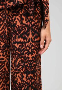 Tissu à motifs marron et noir avec un design organique. Présente une coupe ample avec une taille cintrée et des jambes de pantalon fluides.