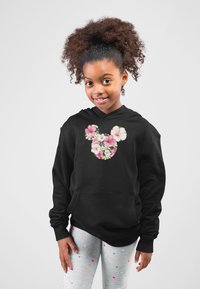 Svart hoodie med blommig Mickey Mouse-logga, prydd med rosa och vita blommor. Matchad med grå tights dekorerade med färgglada prickar.
