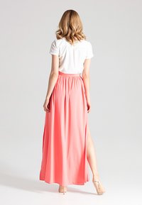 Langer Korallenrock aus leichtem Stoff, mit einem elastischen Bund und seitlichem Schlitz, kombiniert mit einem schlichten weißen kurzärmeligen Oberteil.