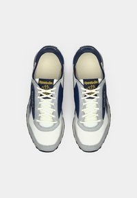 Reebok tenisice s bijelim i mornarsko plavim gornjim dijelom, sivi dodaci i bijele vezice. Okrugli dizajn s teksturiranom gumenom potpeticom.