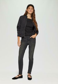 Zwarte bomberjack met rits over een zwart topje, gecombineerd met donkere jeans en zwarte ballerina's. De jas heeft geribbelde manchetten en een getailleerd ontwerp.