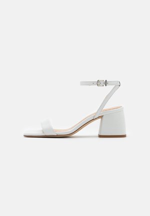 Sandales à talons blancs avec un bout carré, une bride de cheville et une boucle. Présente un talon bloc solide et une texture en cuir lisse.