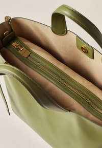 Green leather tote bag with a spacious interior, featuring a zip pocket and beige lining. Accented with gold hardware and smooth edges.