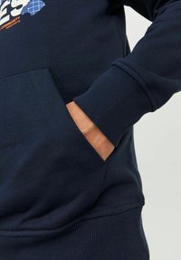 Sudadera azul marino con un bolsillo tipo canguro, puños y dobladillo acanalados, que presenta un diseño gráfico en el frente. Textura de tela de algodón suave.