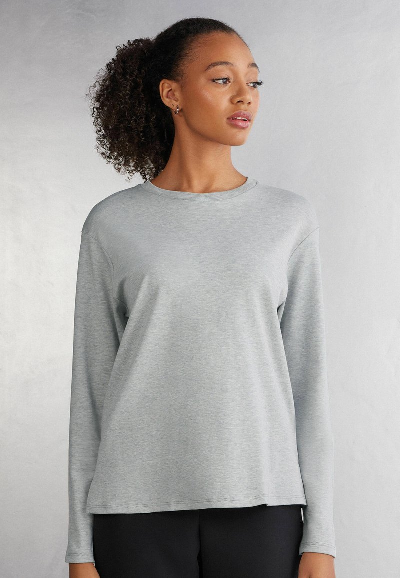 Helles graues Langarmshirt aus weichem Stoff mit Rundhalsauschnitt und lockerer Passform, das minimale Nähdetails und kein Muster aufweist.