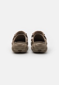 Brown textured clogs with a molded design, open back, and adjustable strap. Features ventilation holes near the heel and rounded toe.