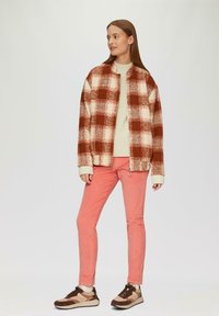 Brązowa i kremowa marynarka w kratę, beżowy sweter, różowe spodnie i brązowe sneakersy. Miękkie tkaniny, luźny krój i kontrastujące kolory.