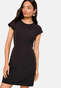 Fekete, rövid ujjú ruha, amely testhez álló felső résszel, finom V-alakú varrással a deréknál, puha textúrával és egyenes siluettel rendelkezik.