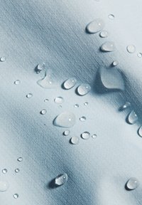 Wassertropfen perlen auf einer glatten, hellblauen wasserabweisenden Stoffoberfläche mit feiner Rastertextur.