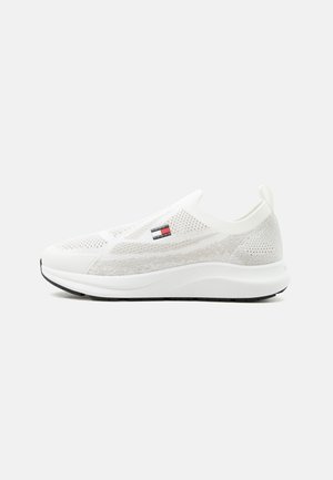 Witte lage slip-on sneaker met gebreide bovenkant, logo patch aan de zijkant, dikke zool en aantreklus bij de hiel.